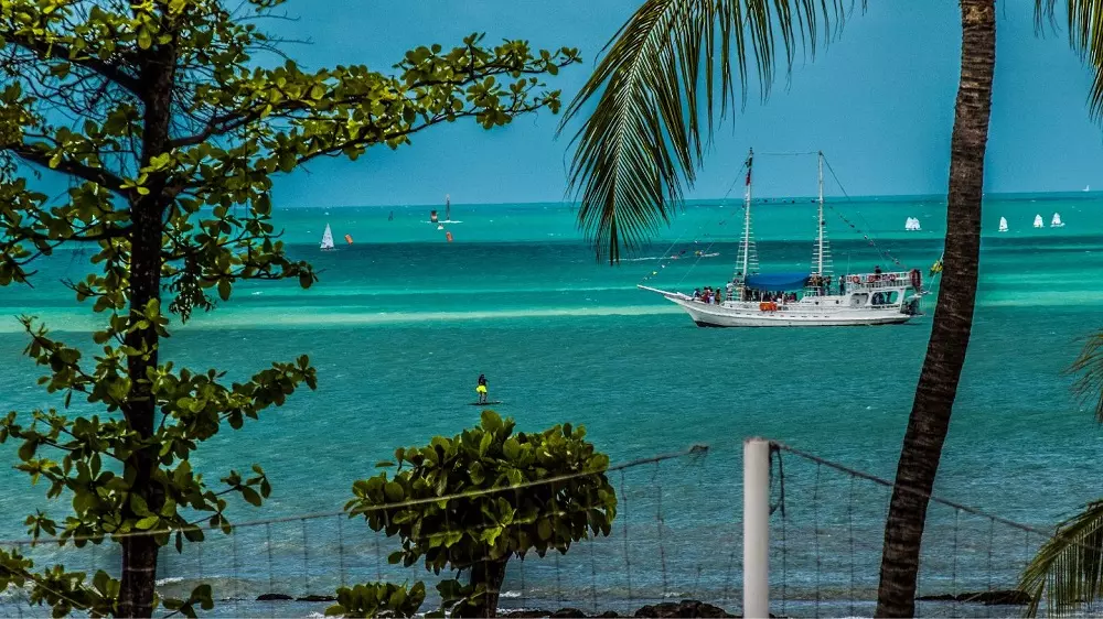 Como é morar na Praia do Futuro em Fortaleza Imagem de praia e mar, com vegetação e barco. Ilustrativo para texto praia do futuro em fortaleza.